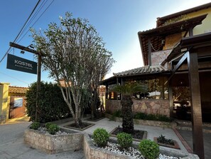 A building with a sign reading 'Kastel Buzios Centro' and a well-maintained garden with various plants and a tree. - Búzios Centro Hotel (Búzios)