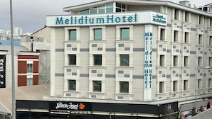 Un hôtel appelé Melidium Hotel, doté d’une façade moderne, de nombreuses fenêtres et d’une enseigne bien visible pour le café Gloria Jean’s.