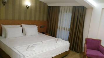 A hotel room with a large bed, a wooden headboard, a nightstand, a purple chair, and a window with curtains.