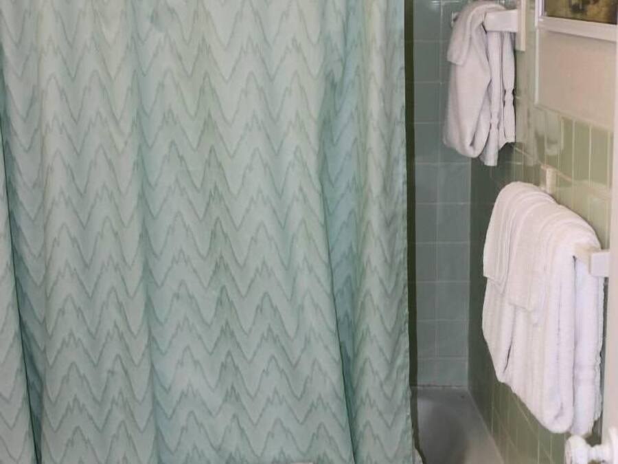 Un baño con cortina de ducha, bañera, inodoro y un perchero con toallas.