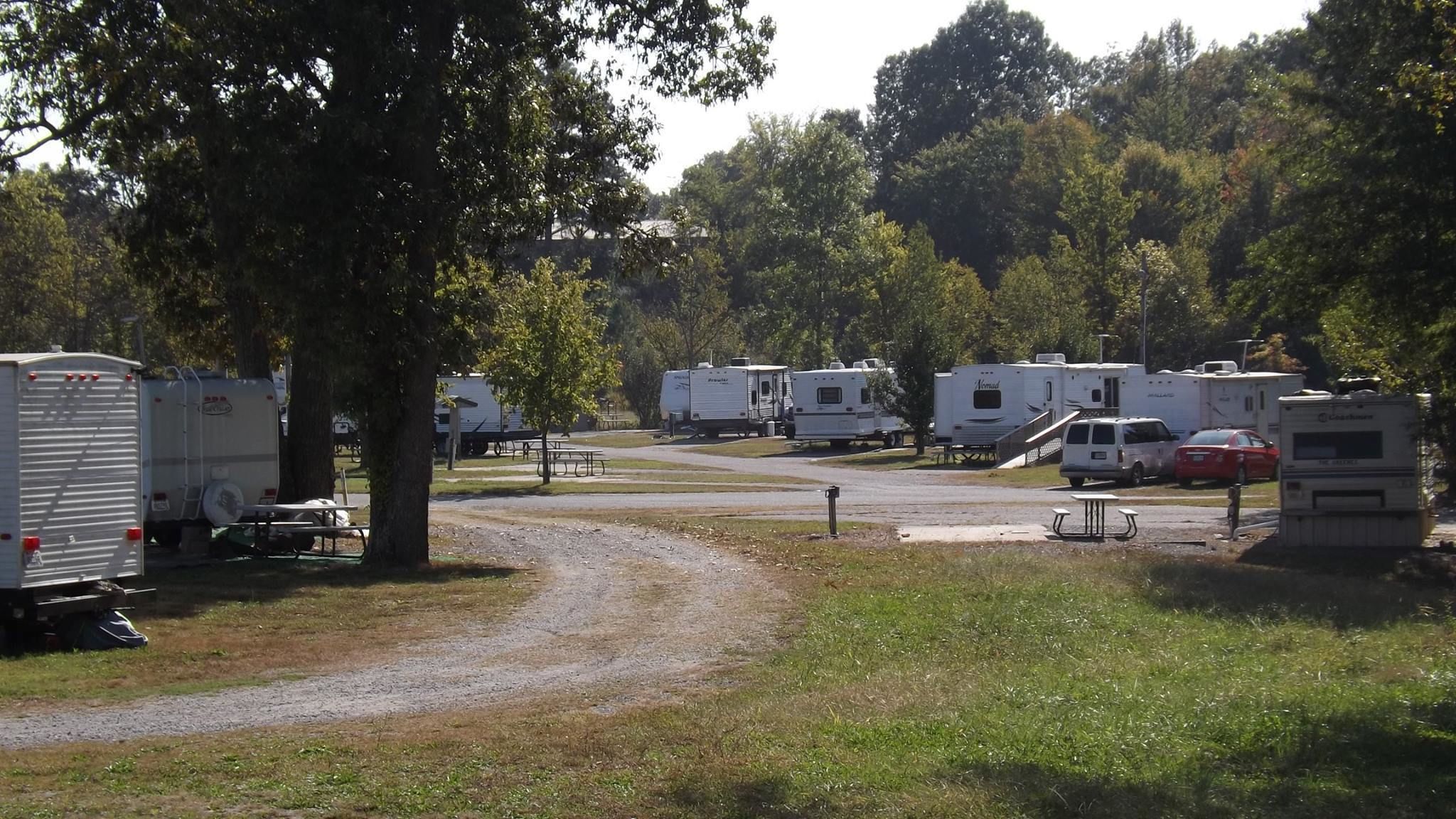 Un camping con vehículos recreativos estacionados en filas, mesas de picnic y un camino de grava.