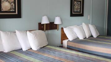 Habitación de hotel con dos camas, cada una con almohadas blancas y ropa de cama a rayas. Hay lámparas de pared y obras de arte enmarcadas sobre las camas.
