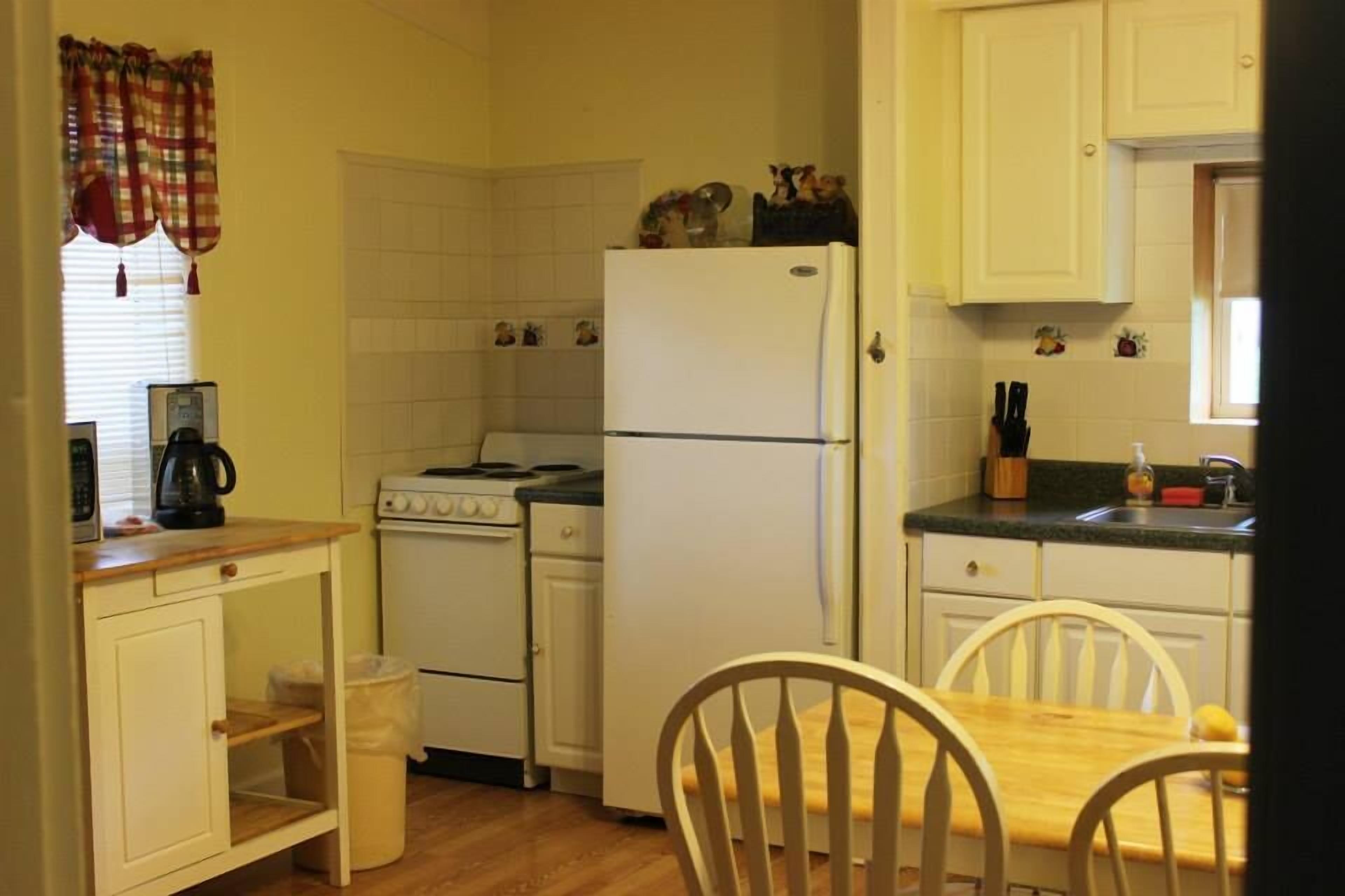 Una cocina compacta con armarios blancos, estufa, refrigerador y una mesa de comedor con sillas.