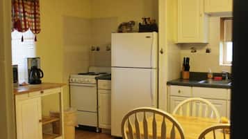 A compact kitchen with white cabinets, a stove, a refrigerator, and a dining table with chairs.