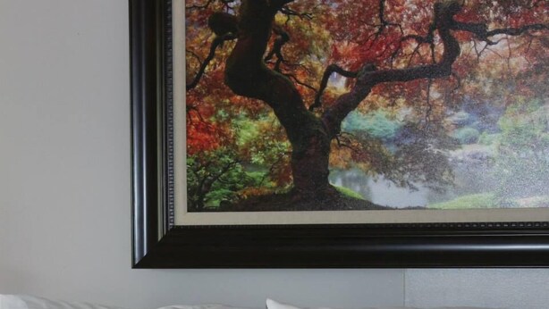 A framed painting of a tree with autumn leaves on a wall above a bed with white pillows. - Kentucky Lake Resort & RV Park (Gilbertsville)