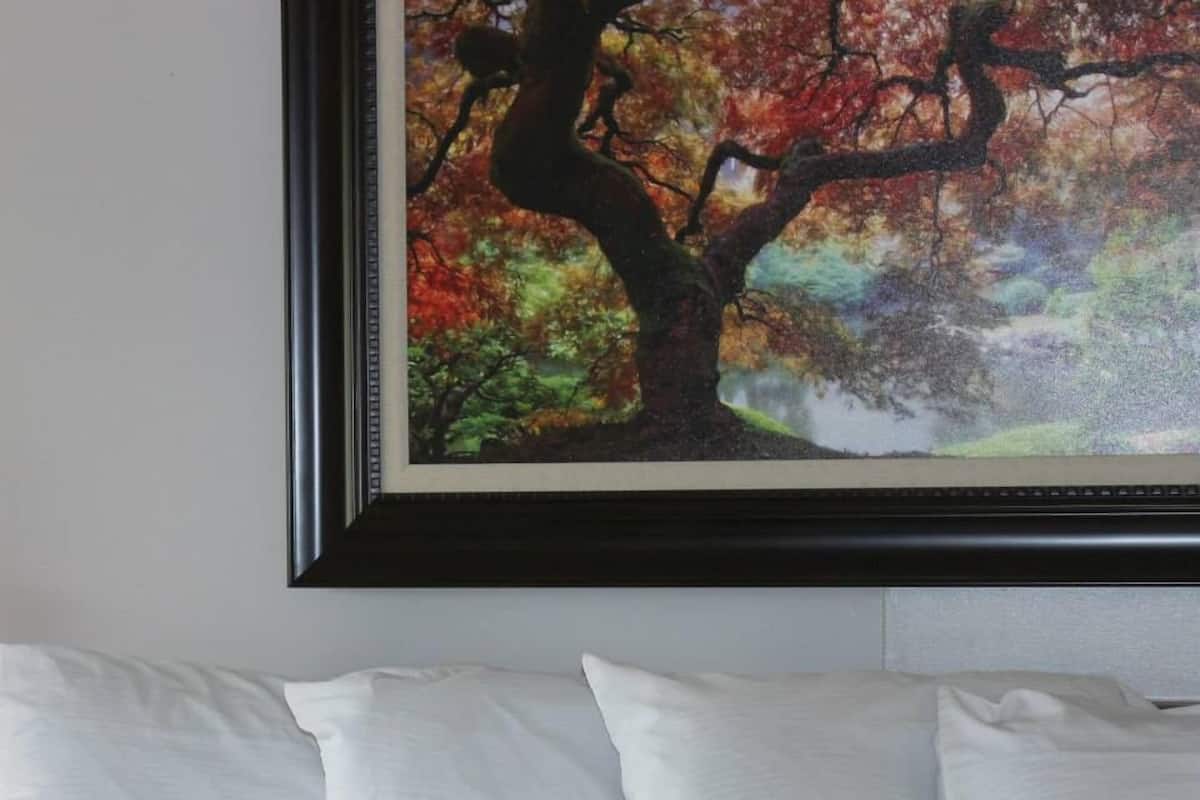 A framed painting of a tree with autumn leaves on a wall above a bed with white pillows.