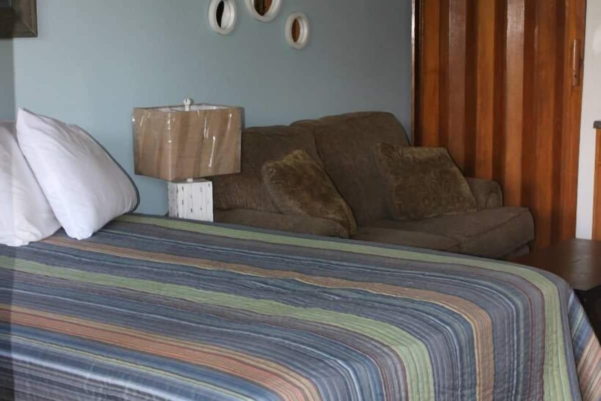A bedroom with a bed, a wooden wardrobe, and a nightstand with a lamp.