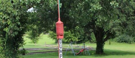 A green and red pole labeled "DUMP STATION" in a grassy area with a playground and a tree in the background.