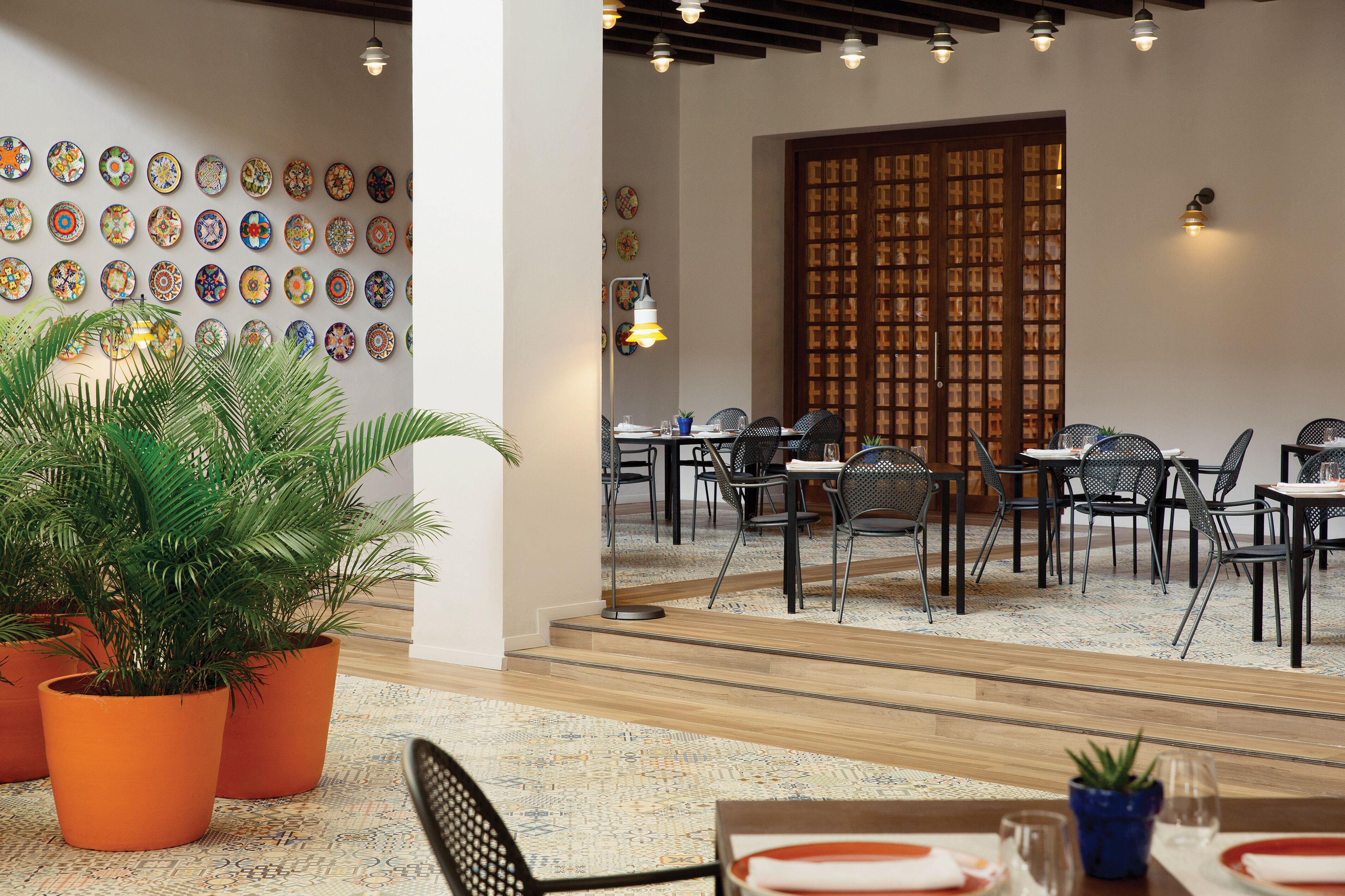Un restaurante con una pared de platos coloridos, plantas en macetas y muebles modernos.