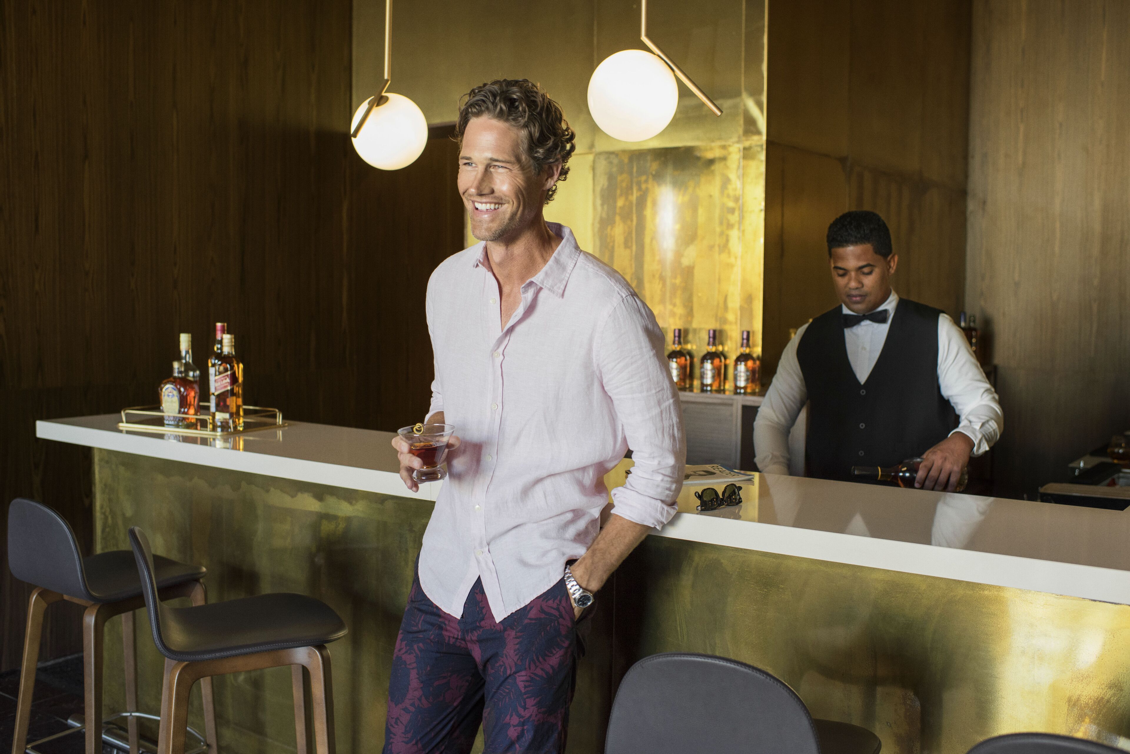 Een bar met een aanrecht, krukken en flessen drank.