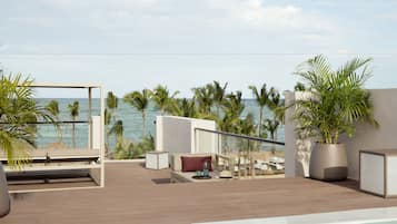 A rooftop terrace with a pool, lounge chairs, and a view of the ocean.