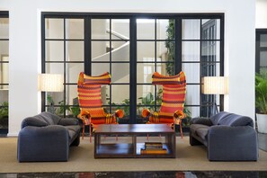 A modern lobby with a sofa, two armchairs, a coffee table, and a large window with a view of a building.