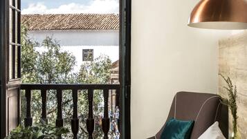 Un balcon donnant sur des immeubles et des arbres, une chaise marron avec un coussin turquoise, un canapé blanc et une suspension en cuivre.