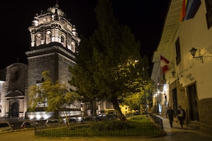 Un edificio histórico con una torre destacada, un paseo empedrado y una bandera.