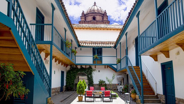 A courtyard with a central staircase, a small table with chairs, and potted plants. - Abittare Hotels (Cusco)