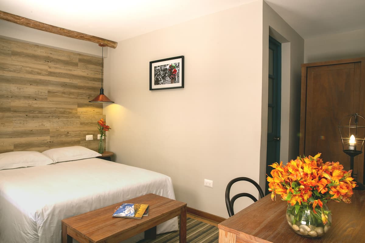 Una habitación de hotel con una cama, una mesita pequeña con un libro, un jarrón de flores y un cuadro en la pared.