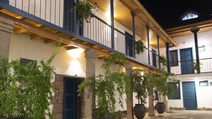 A courtyard with stone flooring, a wooden balcony, and large planters with greenery. - Abittare Hotels (Cusco)