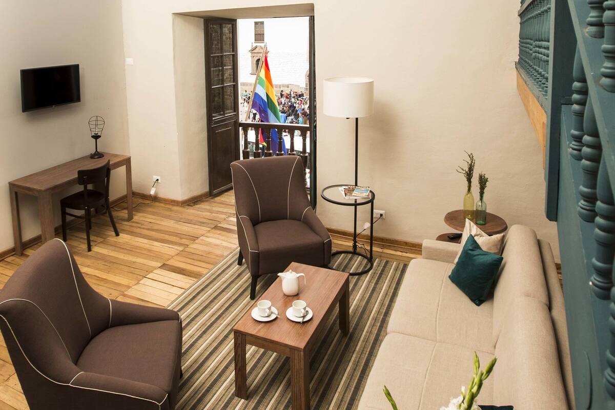 Una sala de estar acogedora con sofá, dos sillones, una mesa de centro, televisor y un balcón con vistas a una bandera.