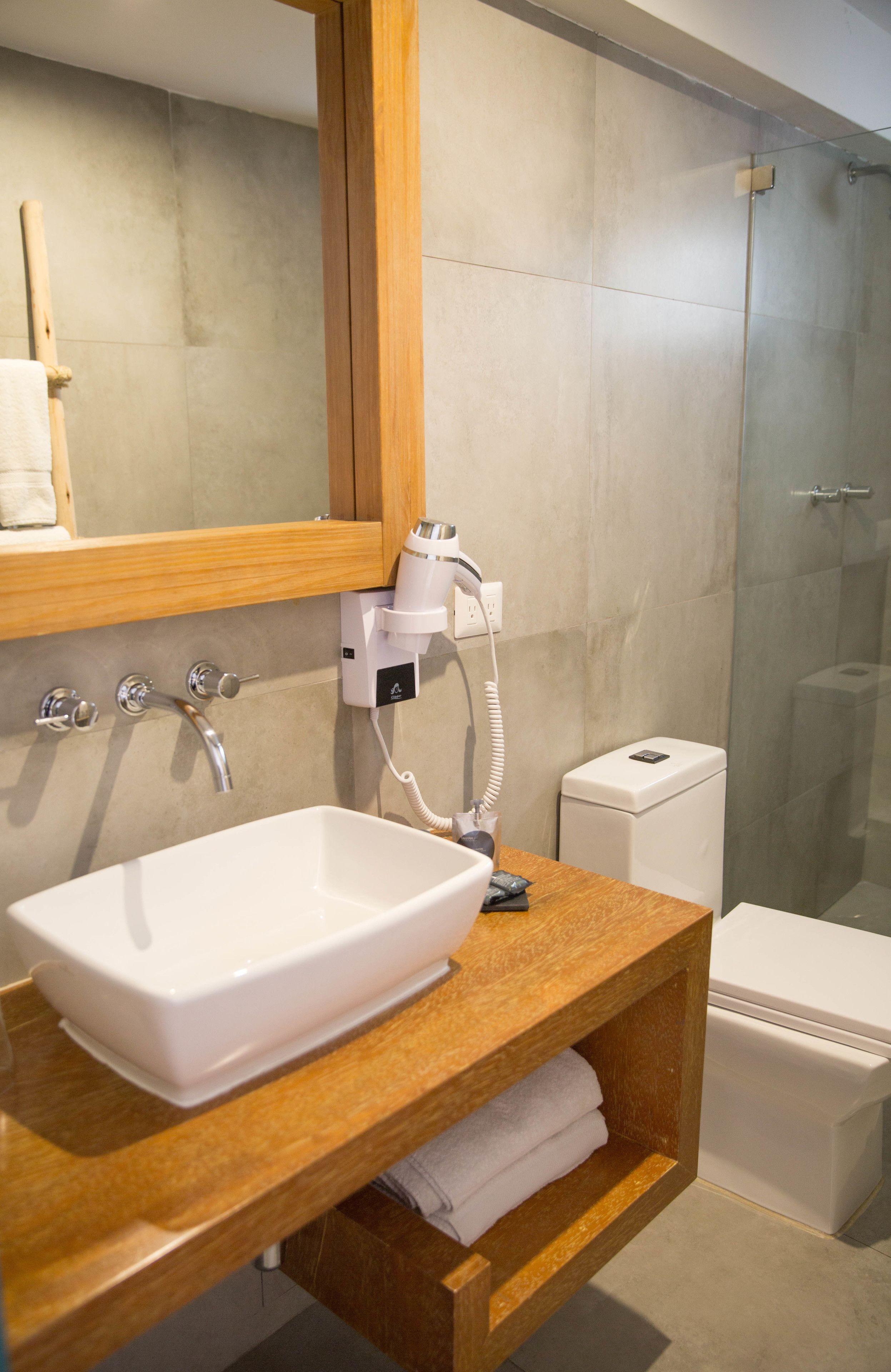 Une salle de bain avec un lavabo blanc, un meuble-lavabo en bois, un sèche-cheveux et une cabine de douche en verre.