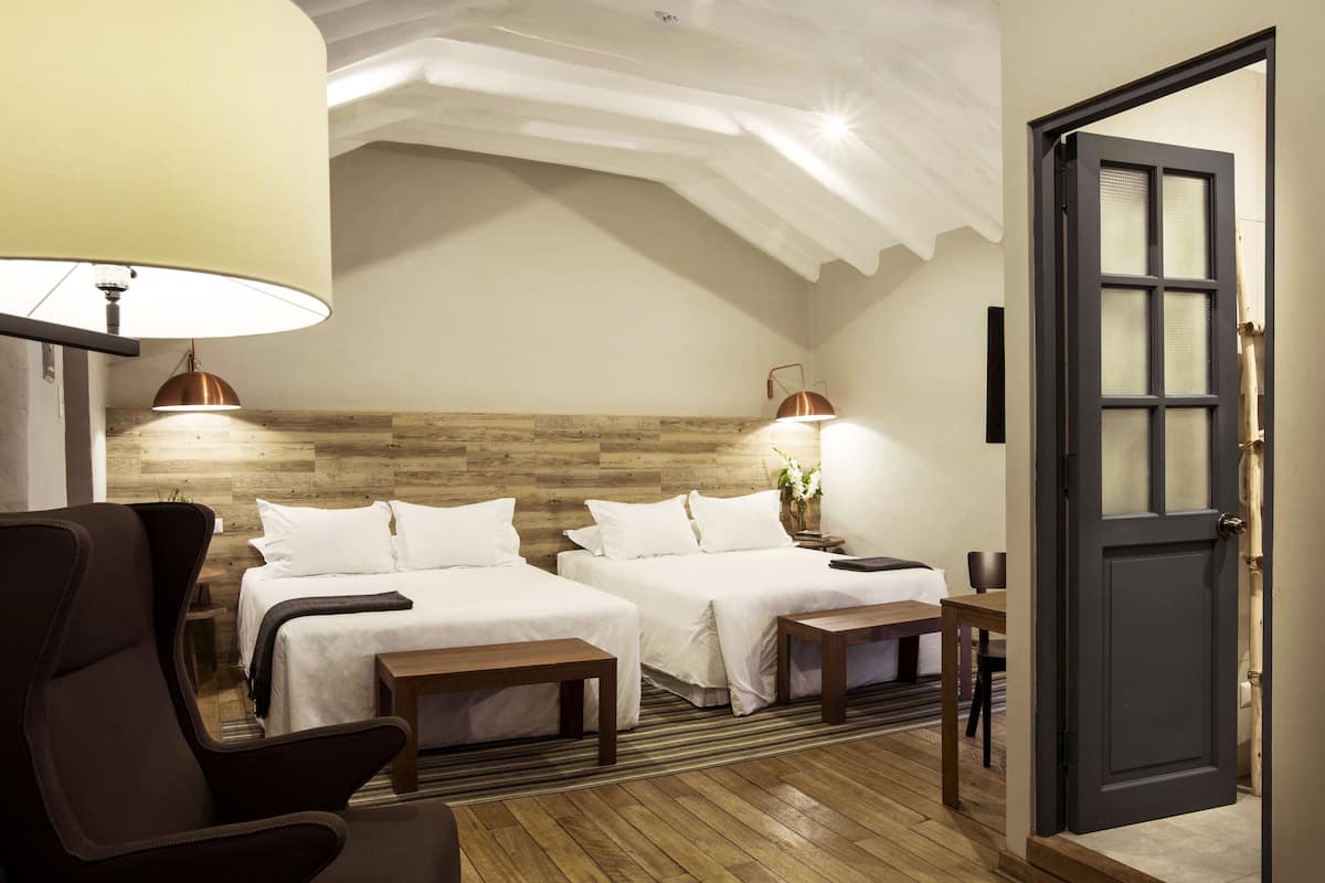 Habitación de hotel con dos camas, cabecero de madera, escritorio y una silla.
