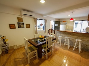 A dining area with a wooden table and chairs, a fruit bowl, and a kitchen in the background. - Iguassu Flats Hotel (Foz do Iguaçu)