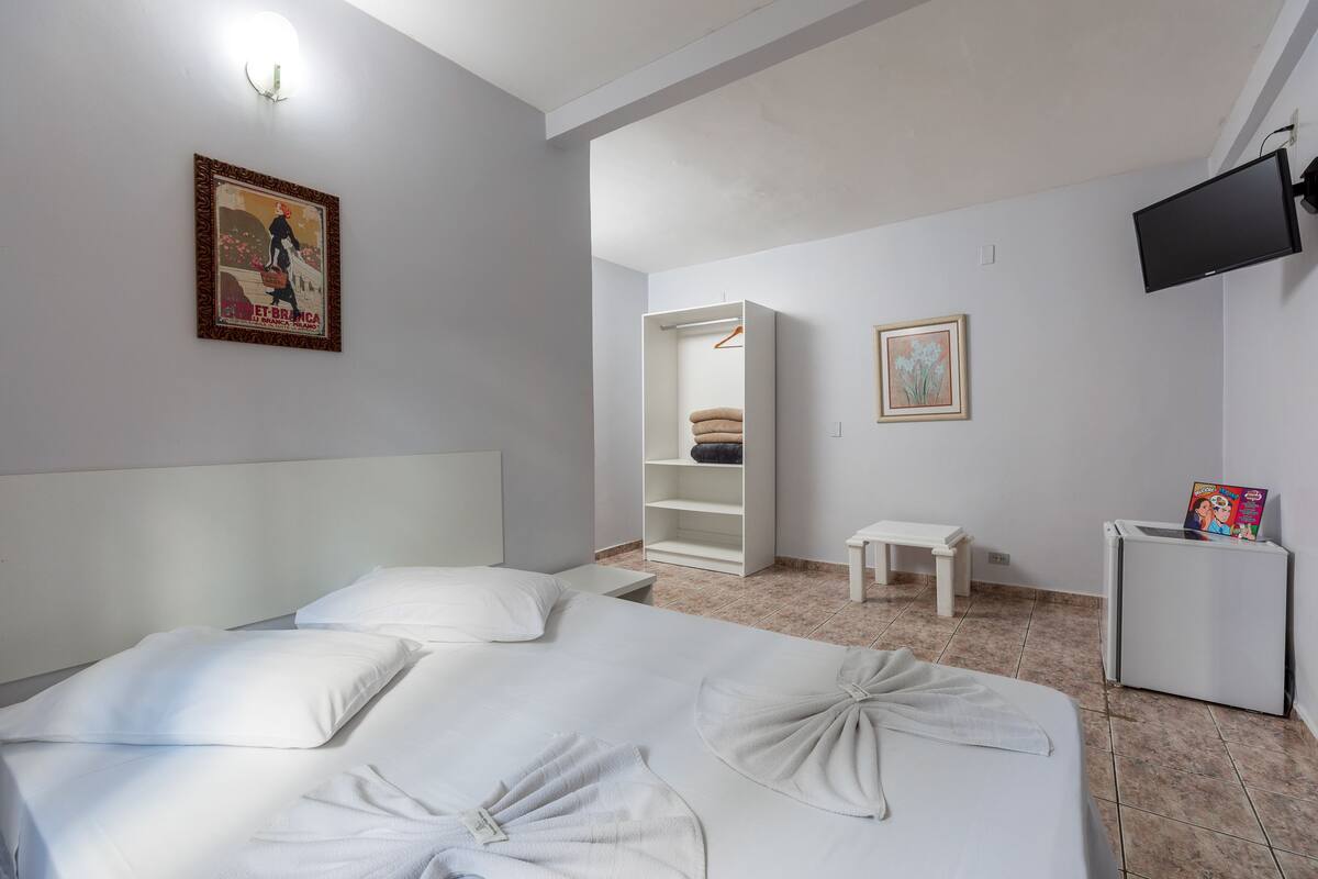 A hotel room with a bed, a wardrobe, a small table, a TV, and a refrigerator.