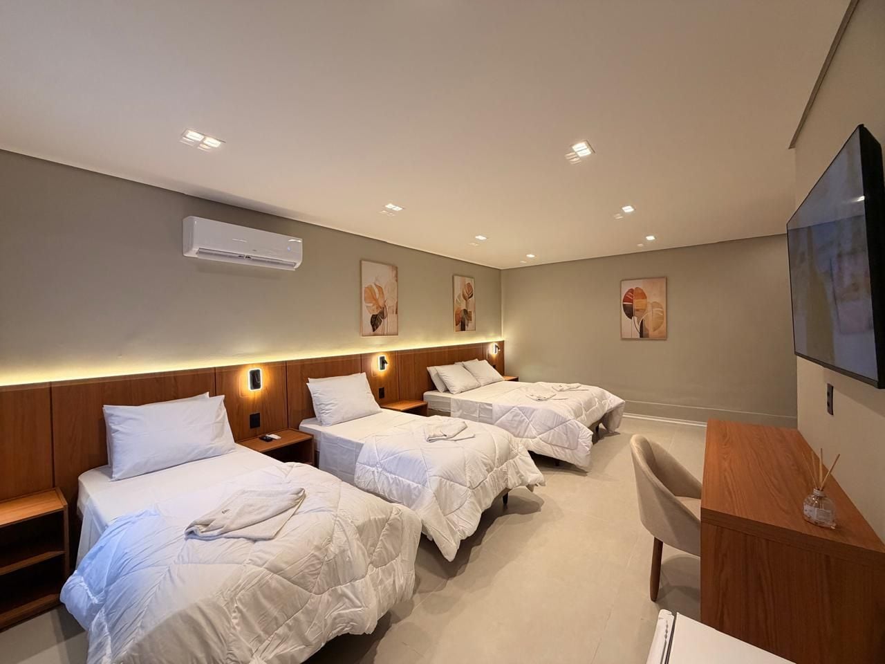 Een hotelkamer met drie bedden, een bureau en een televisie.