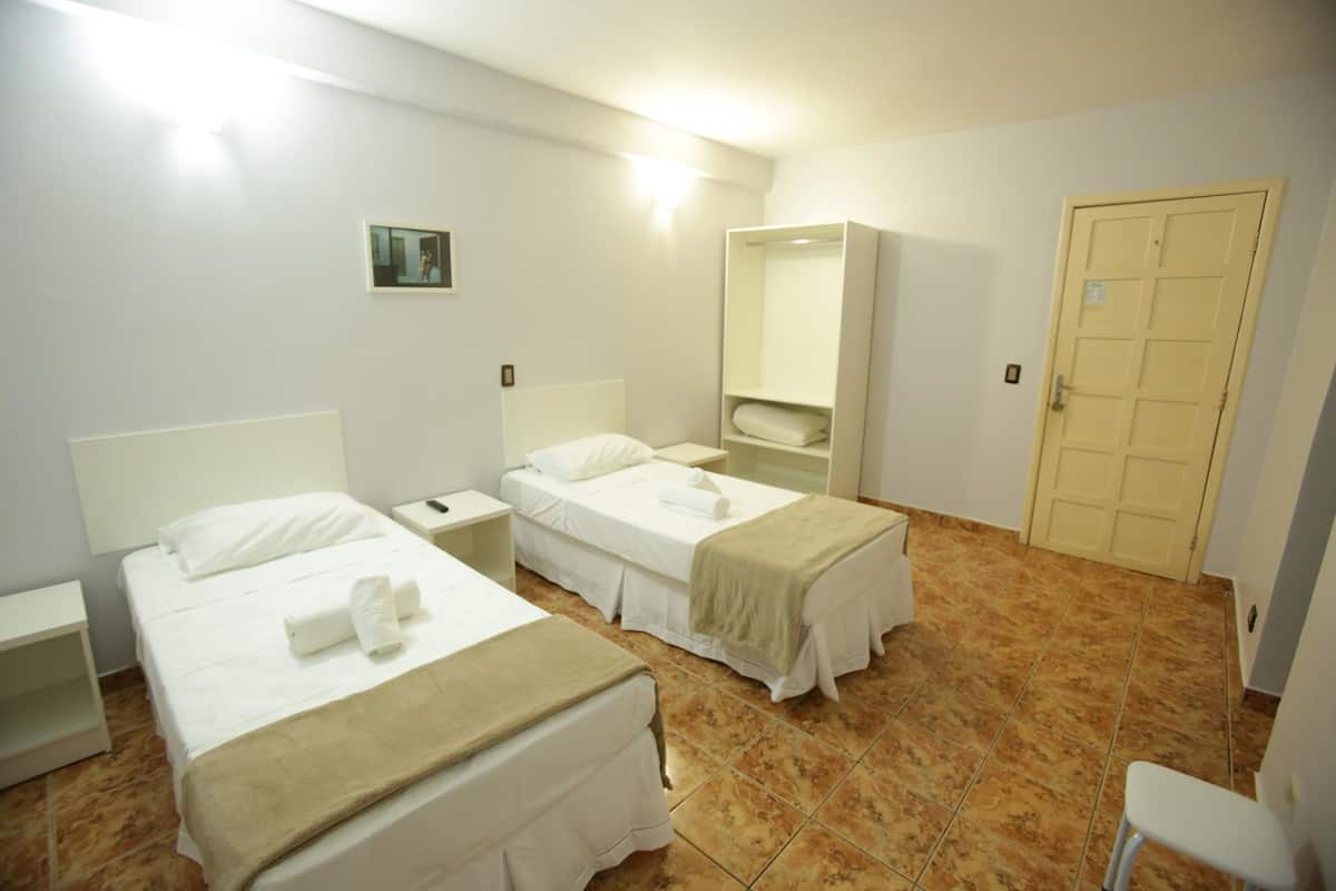 A hotel room with two beds, a bedside table, a mirror, a wardrobe, and a door.