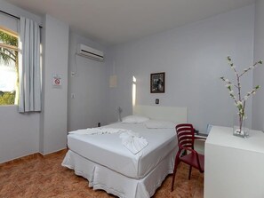 Habitación de hotel con cama, escritorio, silla, aire acondicionado y ventana con cortinas.