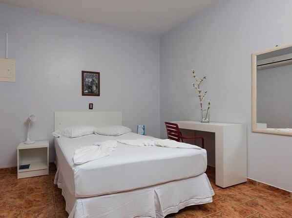 A bedroom with a bed, a desk, a chair, a nightstand, and a wall-mounted mirror.