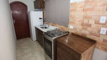 Cozinha compacta com fogão a gás, forno embutido, geladeira branca e armário de madeira.