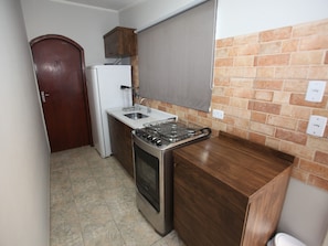 A compact kitchen with a gas stove, a built-in oven, a white refrigerator, and a wooden cabinet. - Iguassu Flats Hotel (Foz do Iguaçu)
