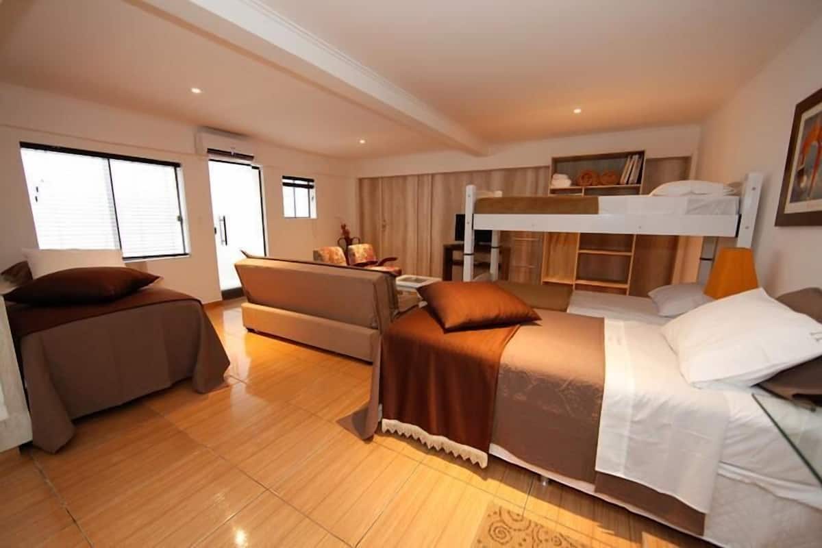 A compact hotel room with a bunk bed, a sofa, a small table, and a chair.