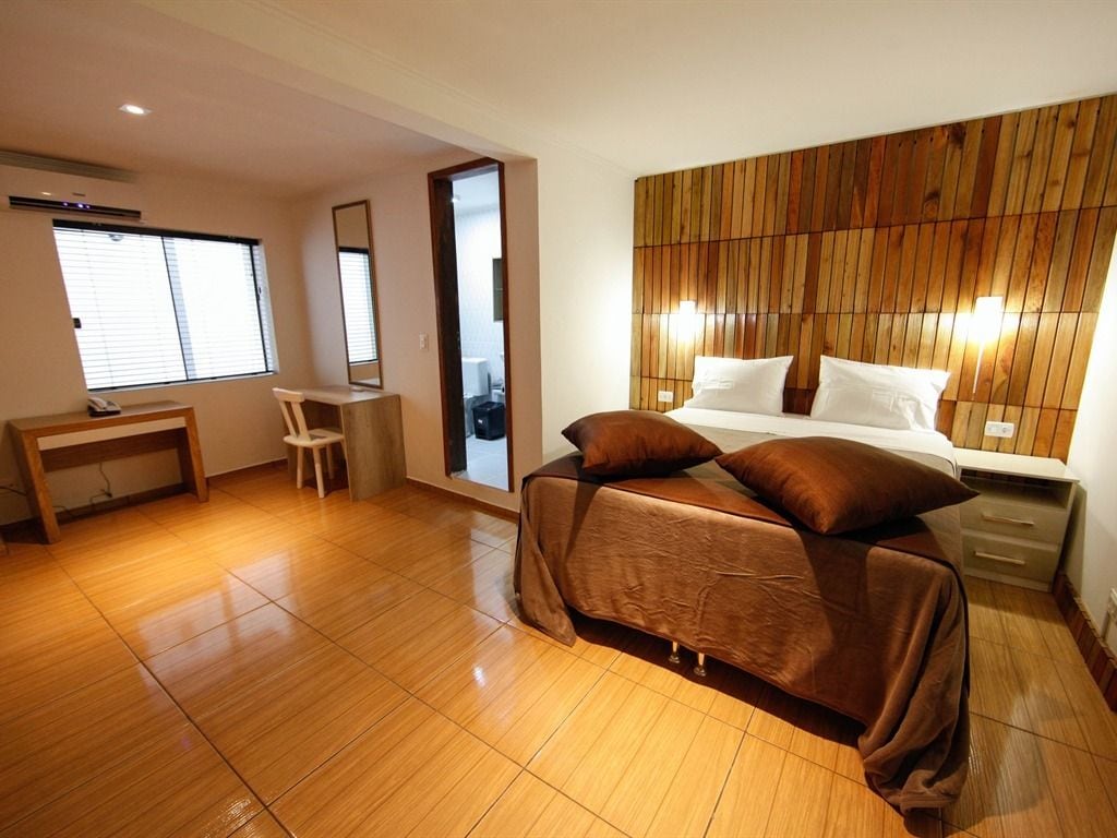 Un dormitorio con cama, mesita de noche, silla y cabecera de madera.