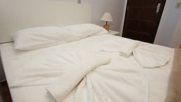 A neatly made bed with a white duvet and pillows, a wooden nightstand with a lamp, and a wooden door in the background.