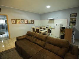 Una sala de estar con un sofá marrón, un área de cocina con refrigerador, microondas y una mesa de comedor.
