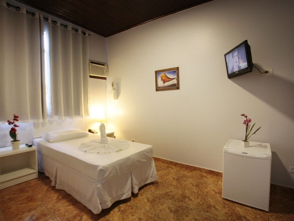 Una habitación de hotel con cama, mesita de noche, lámpara, televisor y un refrigerador pequeño.