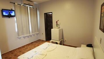 Quarto de hotel com cama, televisão, uma pequena mesa com um vaso e uma porta.