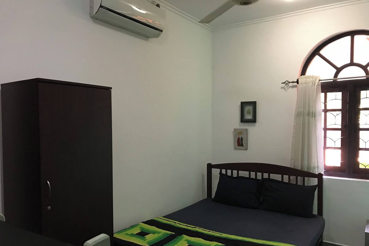 Une chambre à coucher comprenant un lit, une armoire, une fenêtre avec des rideaux et un climatiseur fixé au mur.