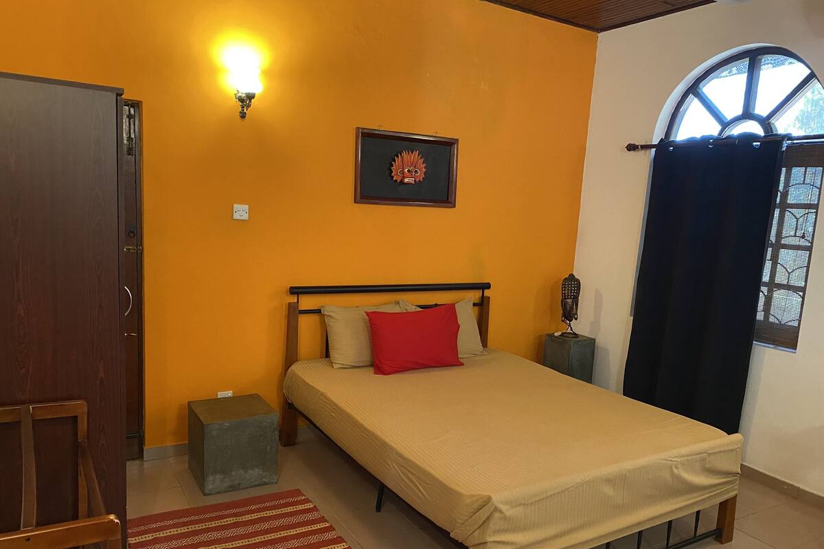 Une chambre à coucher comprenant un lit, une table de chevet, une lampe fixée au mur, un tableau encadré et une fenêtre avec des rideaux.
