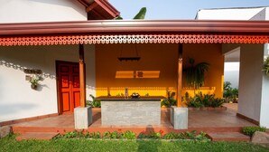 A covered outdoor area with a stone bench, a red door, and potted plants. - Breeze of Paradise (Nugegoda)