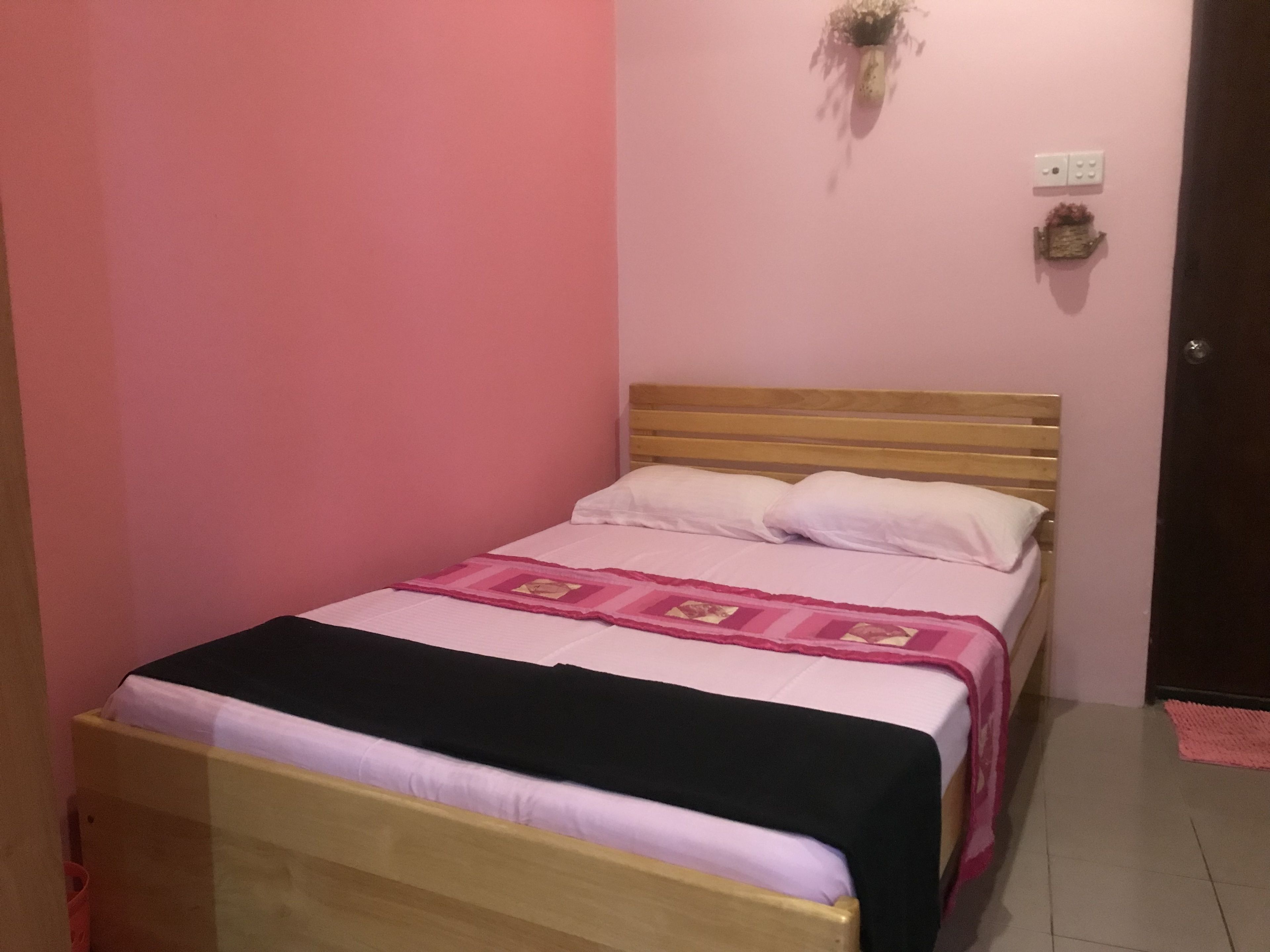 A single bed with a wooden headboard, white pillows, and a pink and black bedspread.