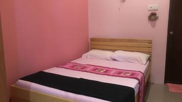 A single bed with a wooden headboard, white pillows, and a pink and black bedspread.