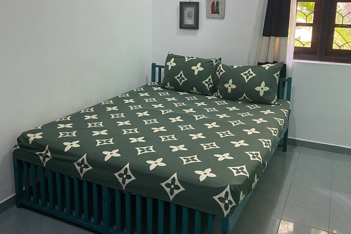 Une chambre à coucher avec un lit, une fenêtre avec des rideaux, un radiateur et un mur orné de deux tableaux encadrés.