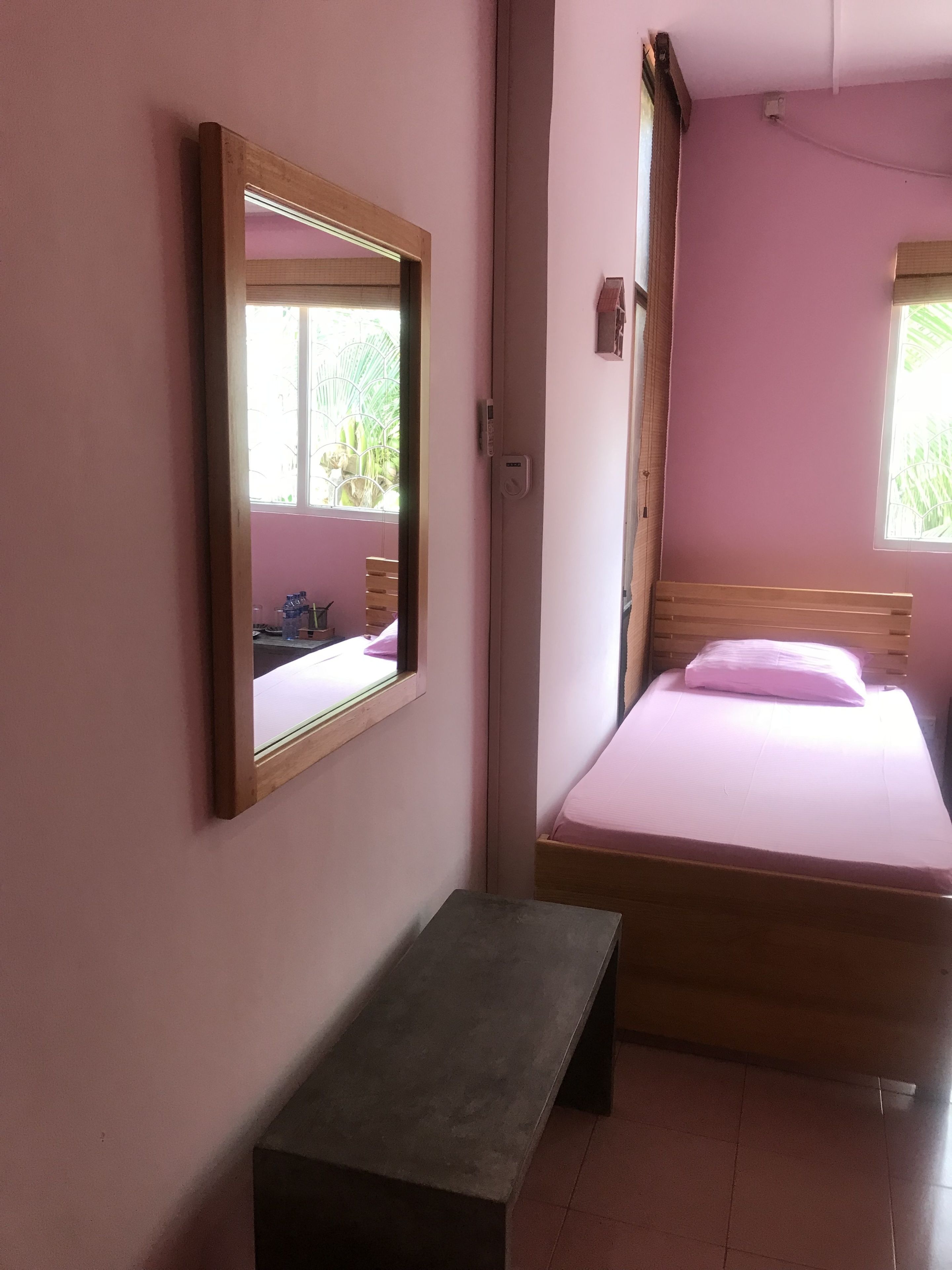 A bedroom with a bed, a bench, a mirror, and a window.