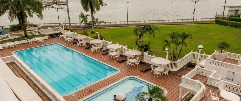 A swimming pool with lounge chairs and tables, surrounded by a well-maintained lawn and palm trees.