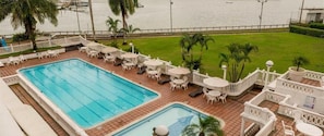 A swimming pool with lounge chairs and tables, surrounded by a well-maintained lawn and palm trees. - Hotel Tequendama Inn Estación (Buenaventura)