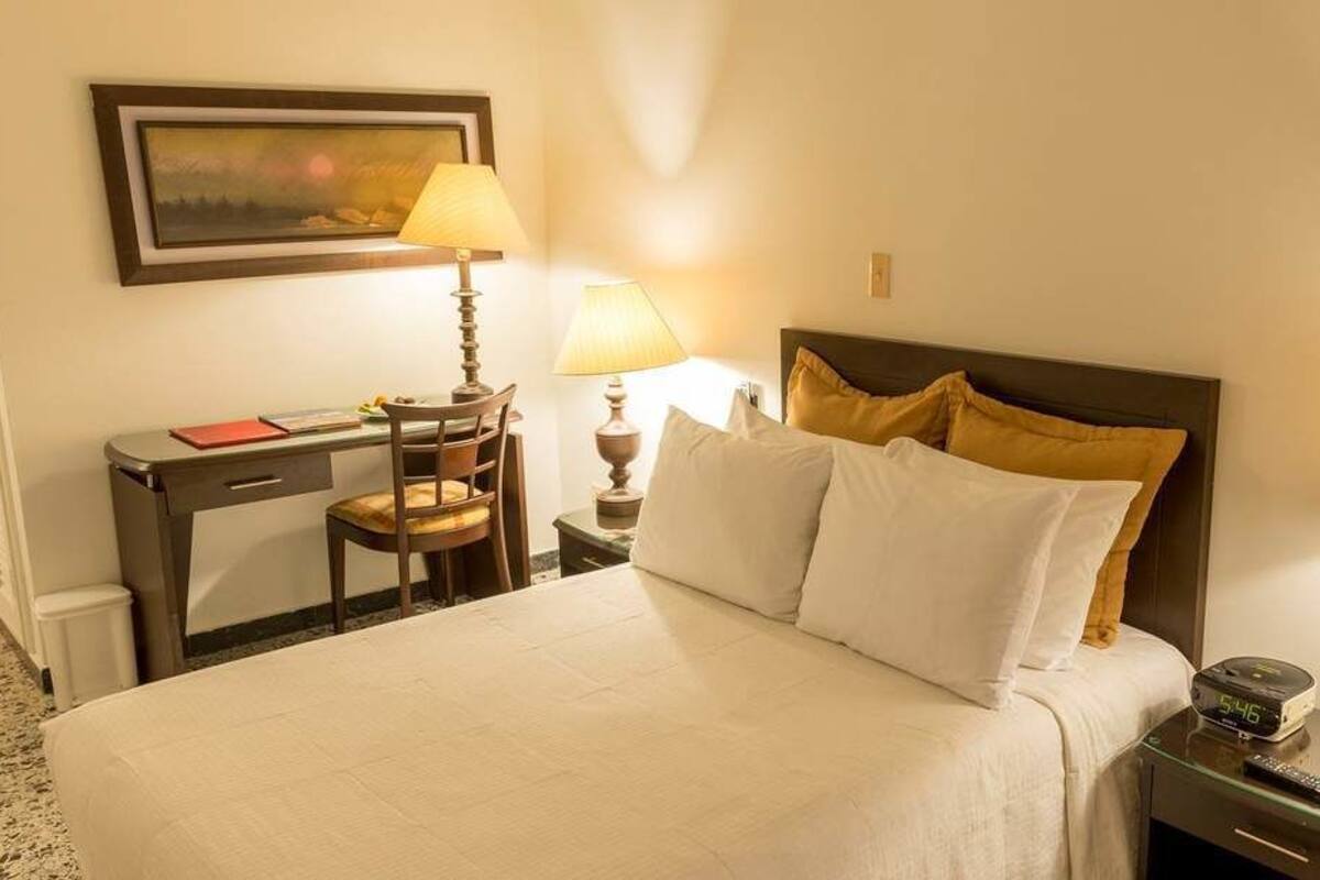 Ein Hotelzimmer mit einem Bett, zwei Nachttischen, einem Schreibtisch und einem Sessel.