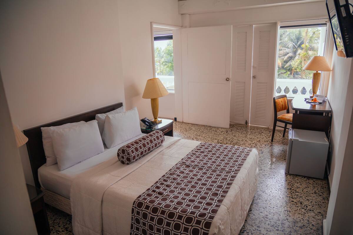 Ein Hotelzimmer mit einem Bett, einem Schreibtisch mit Lampe, einem Sessel und einem kleinen Kühlschrank.