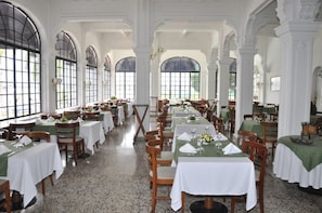 A dining area with long tables, chairs, and large windows.